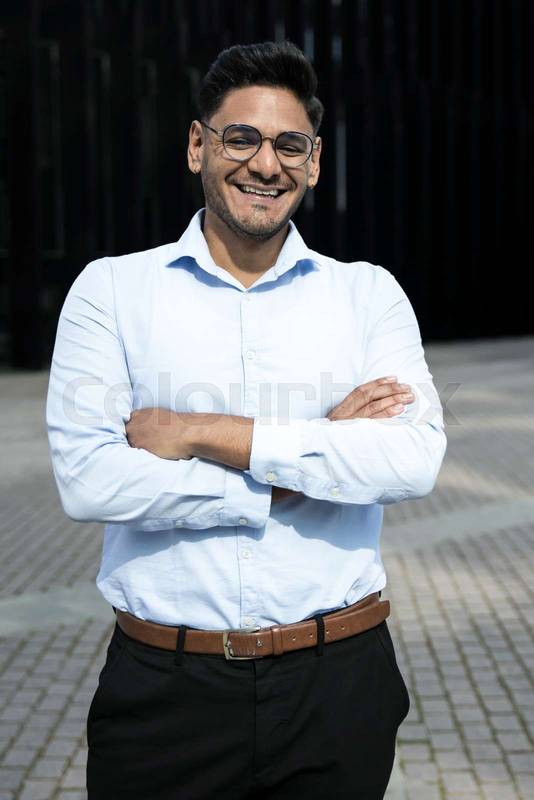 Smiling businessman arms crossed wearing glasses. Cheerful executive laughing in the street.
