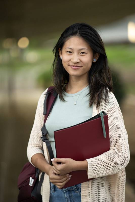 Handsome satisfied student holding a notebook looking at camera.Relaxed and happy woman standing outside with folder in her hands.