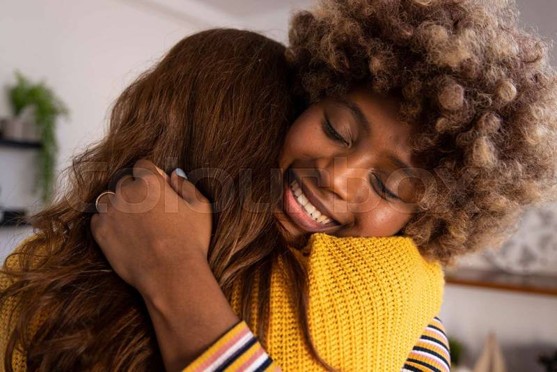 Carefree and joyful female couple hugging each other at home. Head shot close up happy multiracial girl cuddling smiling female friend.