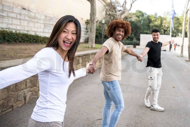 Three diverse and confident friends holding hands together. Multiracial group of people laughing and holding hands in a line. Focus on first woman.
