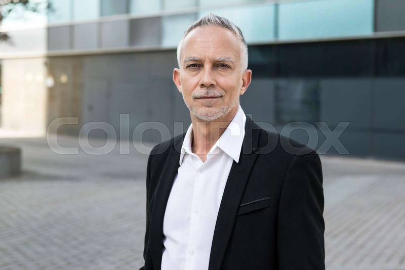 Portrait of a handsome senior businessman standing at outdoors. Mature corporate confident executive looking at camera. Financial concept 