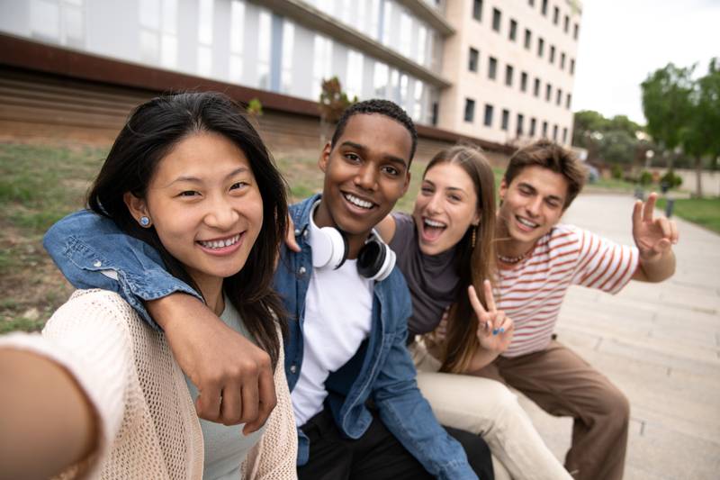 Happy joyful group of friends taking a selfie smiling. Multicultural young carefree people having fun and taking pictures outside.