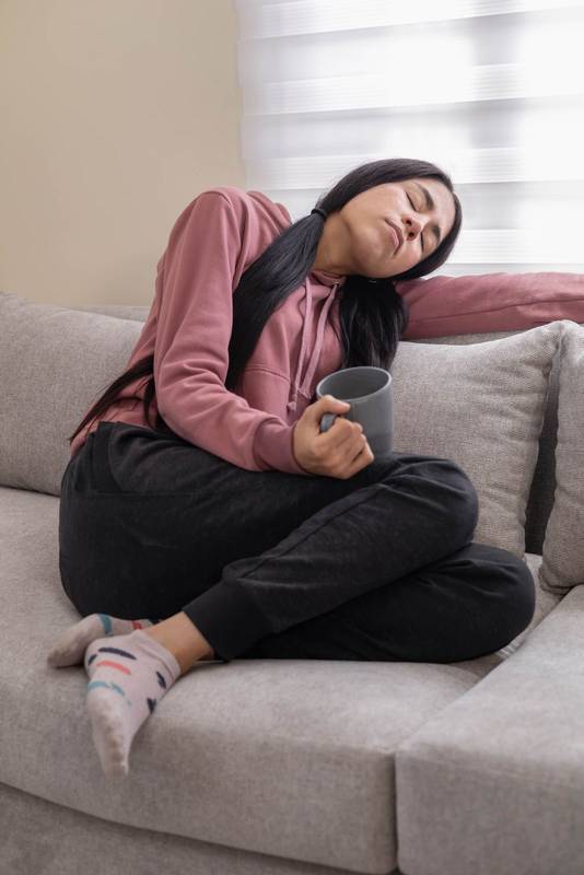 woman seated on a sofa, sipping coffee and enjoying a peaceful, relaxing time