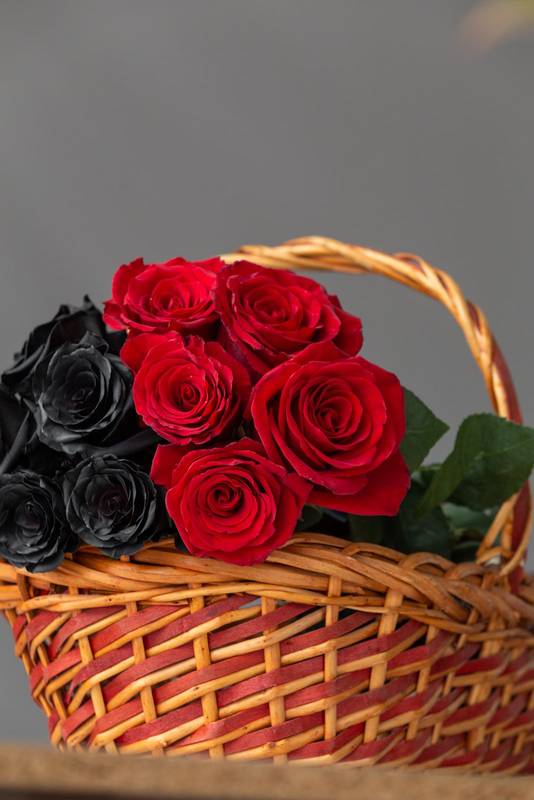 bouquet of flowers with black and red roses inside a wicker basket, beautiful decoration with beauty of nature on a table