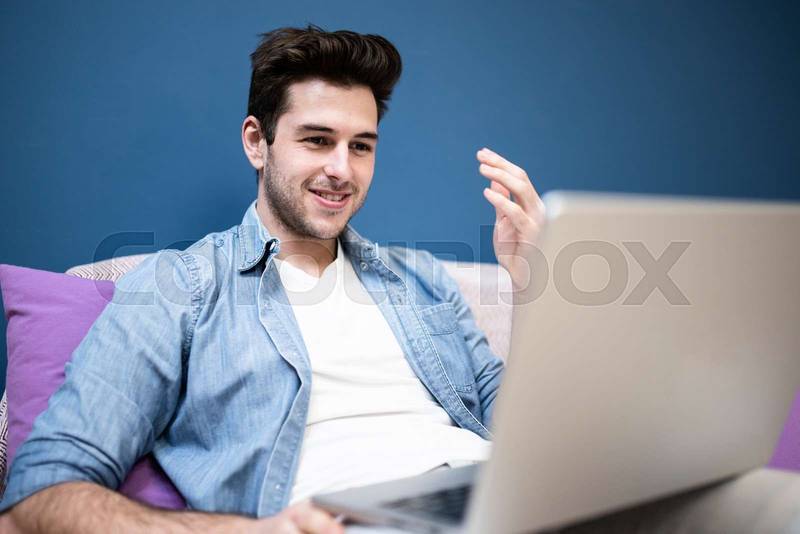 Excited handsome young man looking at laptop screen sitting on cozy sofa at home. Student reading amazing news on computer. Technology concept