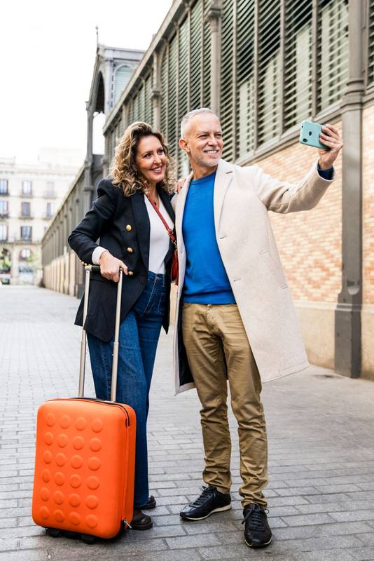 Happy mid adult tourist couple travelling together taking a selfie with her luggage. Affectionate senior husband and wife taking a picture during a weekend romantic trip in european city