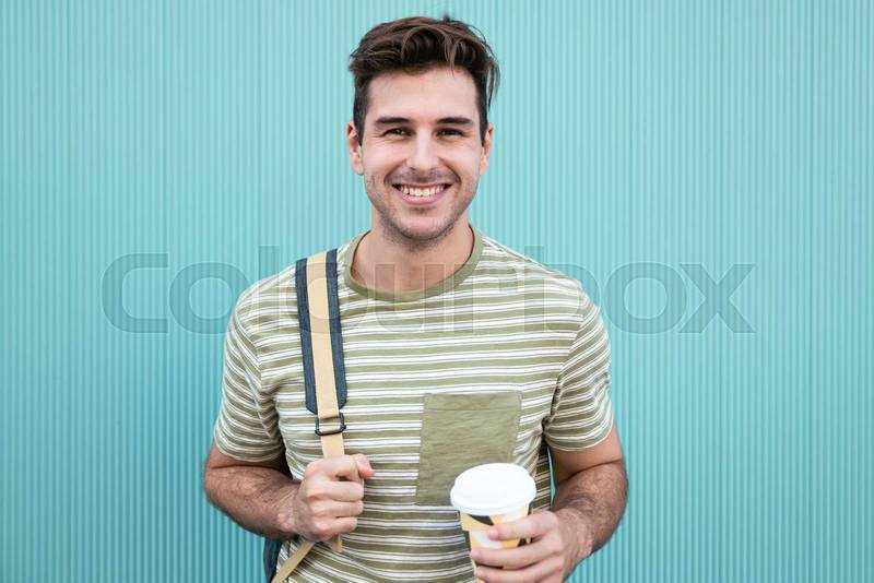 Portrait of handsome happy student smiling and drinking a take away coffee at a green wall.