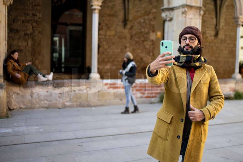 happy bearded young man taking a selfie in the old city - Young man using mobile phone at historic building. Vacations concept