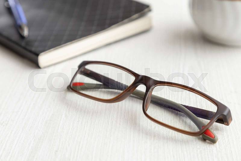 glasses on a wooden desk in the day, next to a notebook with a pen
