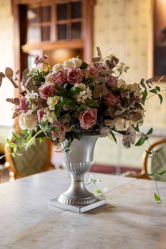 Soft pink roses and green leaves arranged in a refined silver vase