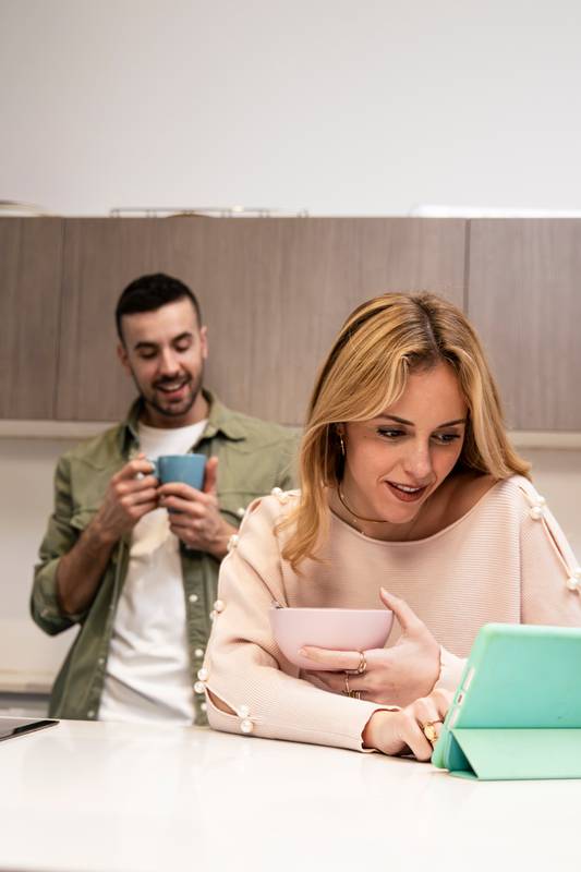 Happy carefree couple planing together with tablet and at home. Smiling man talking with woman using online device in the kitchen.