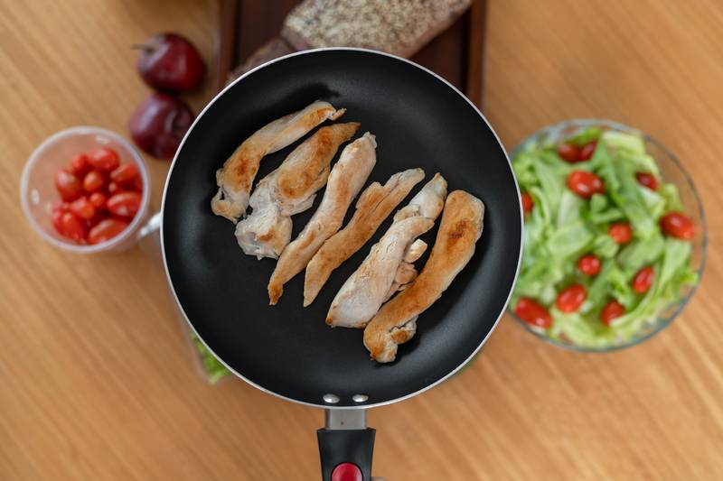 fried chicken pieces sizzling in a pan, with a refreshing tomato salad