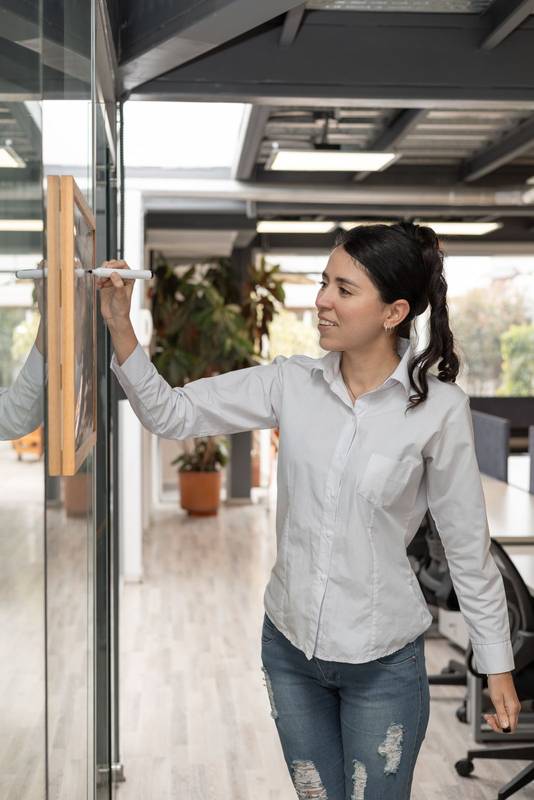 writes notes on a whiteboard during a meeting. The office setting highlights creativity, teamwork