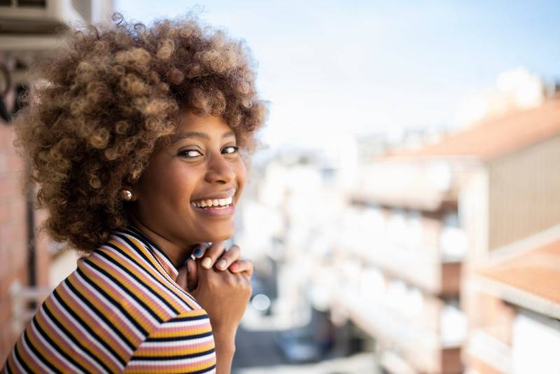 portrait of young smiling woman looking at camera standing outdoors. Closeup of beautiful happy girl in the city with hands on chin. 
