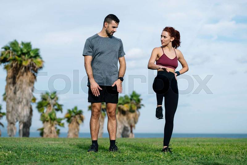 Athletic male looking at female coach in sportswear training workout outside. Lovely young adult couple warming up in park after running together. 