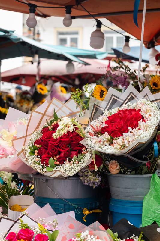 flower bouquets with red roses, white blooms, and sunflowers arranged in buckets at an outdoor flower market