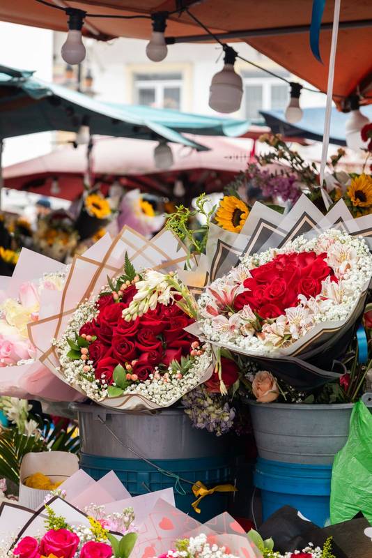flower bouquets with red roses, white blooms, and sunflowers arranged in buckets at an outdoor flower market