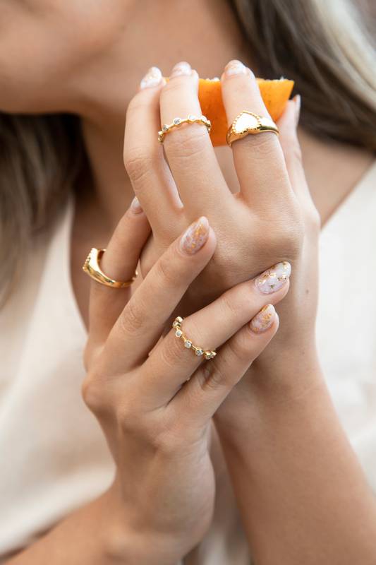 hands of a person holding a piece of citrus fruit, wear various gold rings, modern jewelry