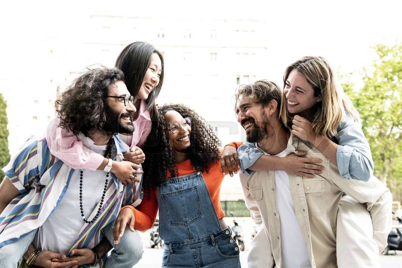 Multiracial group of friends giving piggyback ride and looking each other. Diverse young women and men hugging each other laughing and carefree staring at each other outside.