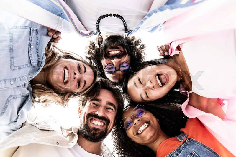 Low view of a multiracial group of young people standing in circle laughing and staring at camera. Diverse happy millennials in circle looking down and having fun.
