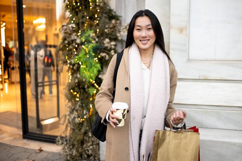 Young smiling woman standing in a shop with a cup of coffee during winter . Happy girl carrying shopping bags looking at camera.