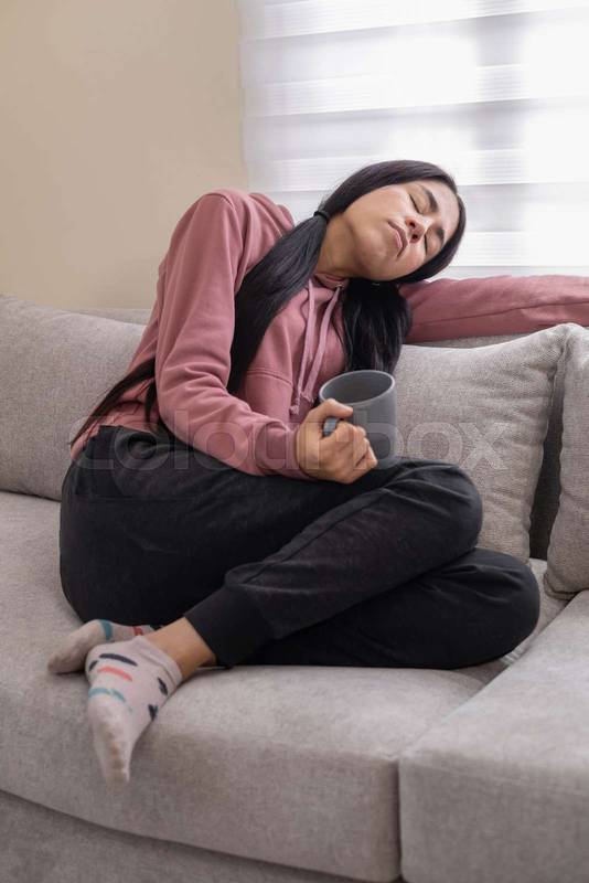 woman seated on a sofa, sipping coffee and enjoying a peaceful, relaxing time