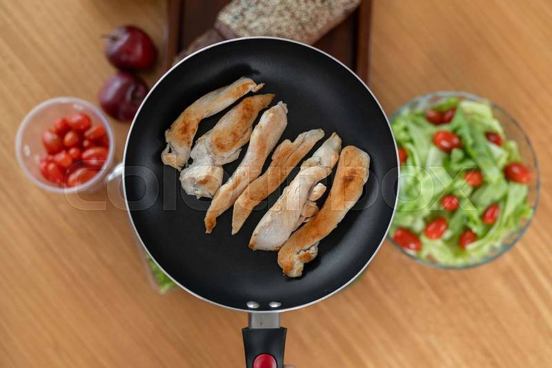fried chicken pieces sizzling in a pan, with a refreshing tomato salad