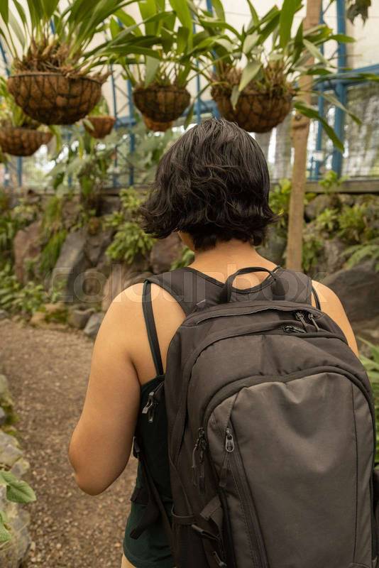 person from behind with a backpack walking along a path in the middle of a garden, lifestyle of a tourist