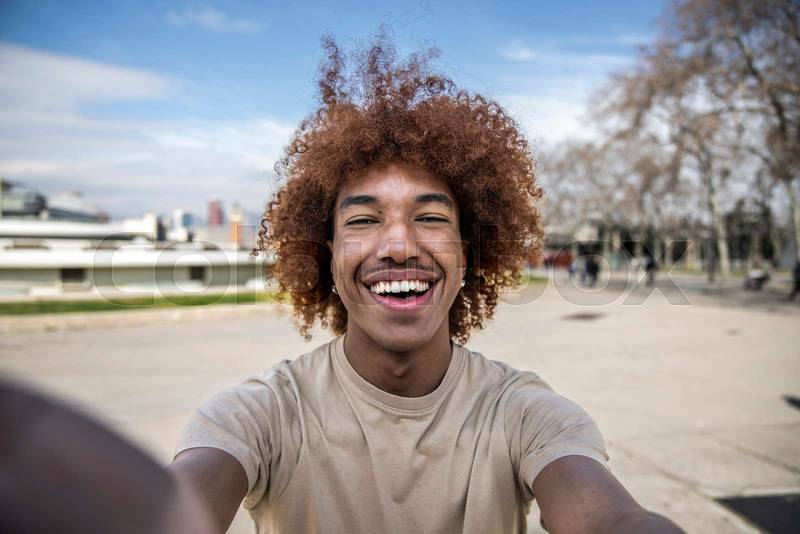 Happy handsome man smiling relaxed and looking at camera in the street taking a selfie. Relaxed happy man laughing and staring and holding the camera standing outdoors.