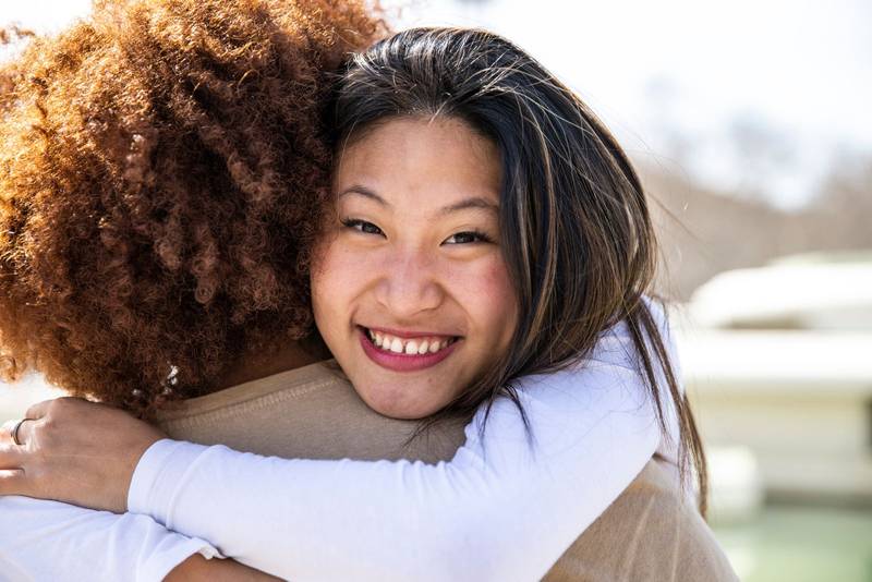 Close up of a young happy woman hugging a curly hair man. Lovely lady smiling while embracing a guy outdoors.