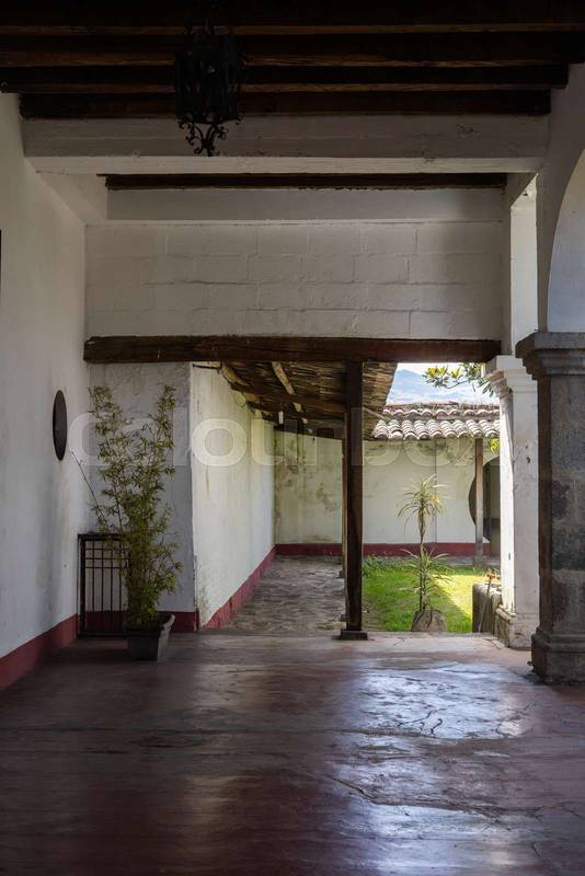 Traditional Ecuadorian hacienda corridor with wooden beams, stone details, and view of a small courtyard garden