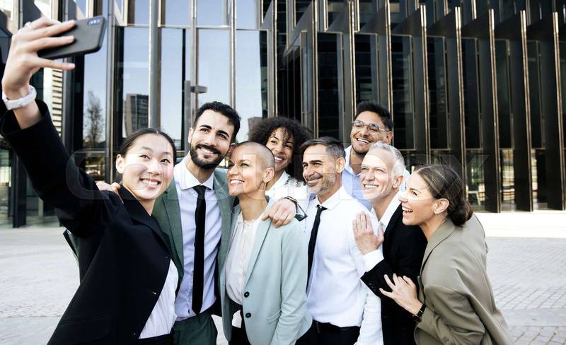 Multiracial group of cheerful and successful business people taking a selfie outside. Diverse office colleagues laughing taking a picture together smiling in the street.
