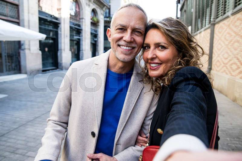 Affectionate happy mid adult couple taking selfie together on the street looking at camera. Lovely happy senior man and woman having fun together taking a photo in a weekend trip.