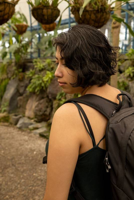 female traveler using a suitcase walking on a garden path surrounded by nature