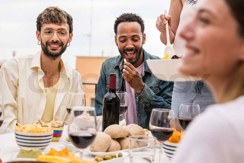 Happy group of friends eating and drinking in a terrace table. Young relaxed people having rooftop dinner party.