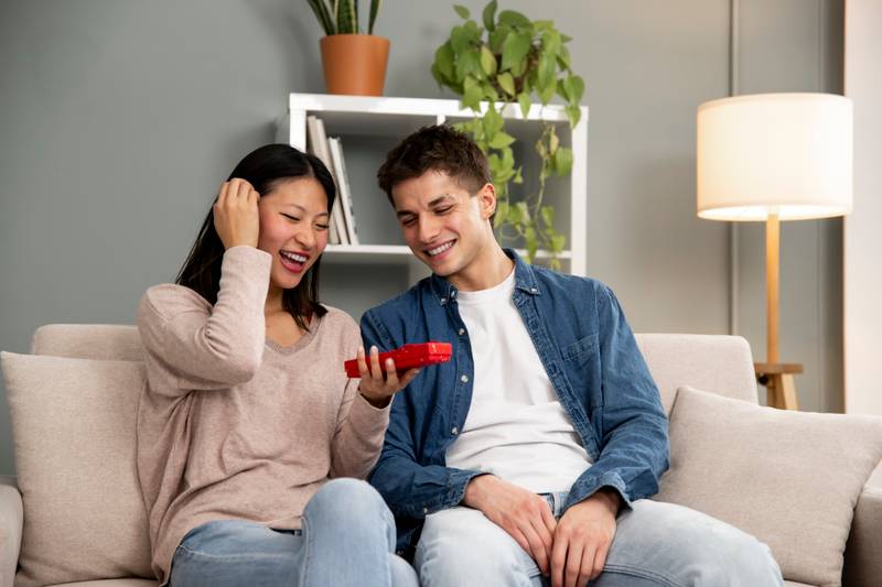 Young diverse couple with mobile phone laughing on sofa. Handsome woman and man sharing smartphone sitting on a couch in their living room.
