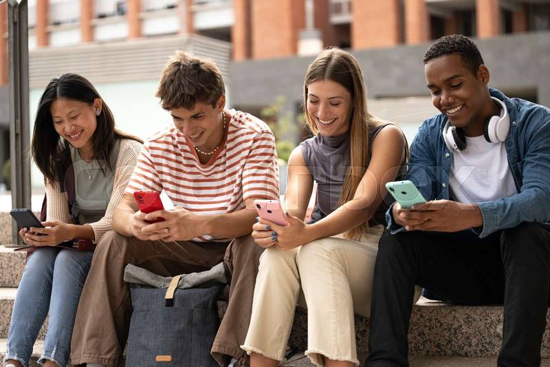 Multiracial young people sitting in stairs while texting.Cheerful group of friends using their phones in the street.