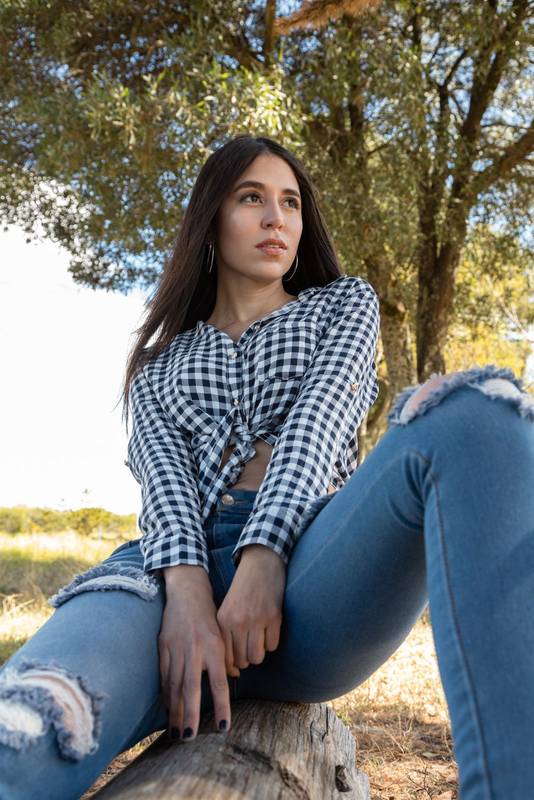 sitting on a tree branch a beautiful young woman with long black hair, wears a casual plaid blouse