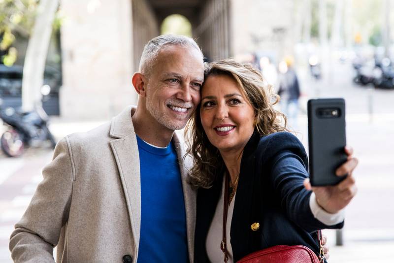 Joyful mid adult handsome couple having fun taking a selfie together in the street. Affectionate senior husband and wife taking a picture during a romantic date in a city.