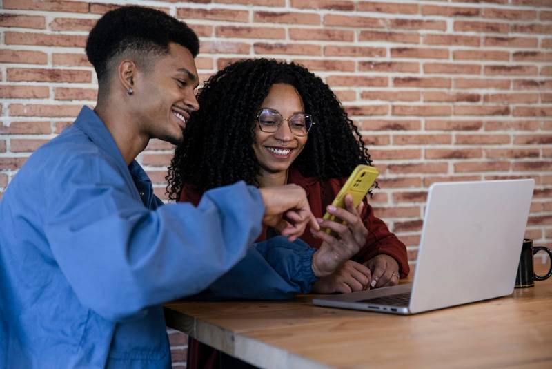 Happy diverse couple buying online investments and financial real estate at home. Husband and wife with credit card and smartphone looking for a new house.