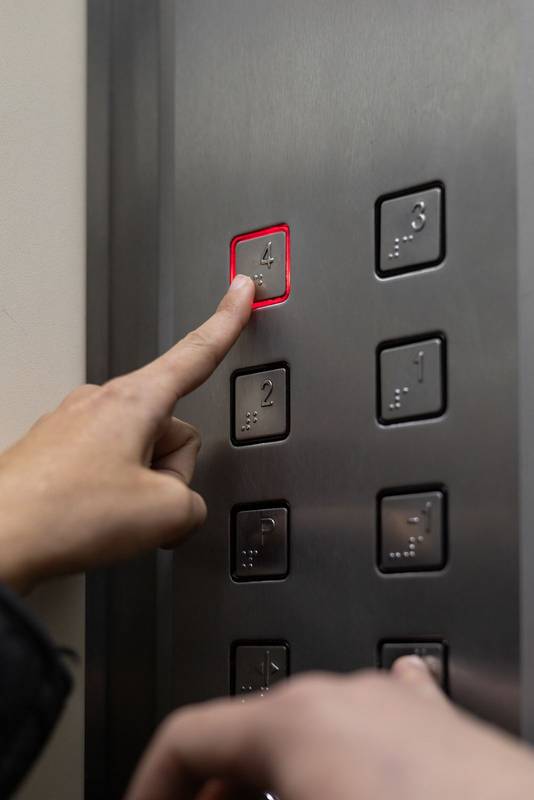finger pressing several elevator buttons, highlighting the metallic texture