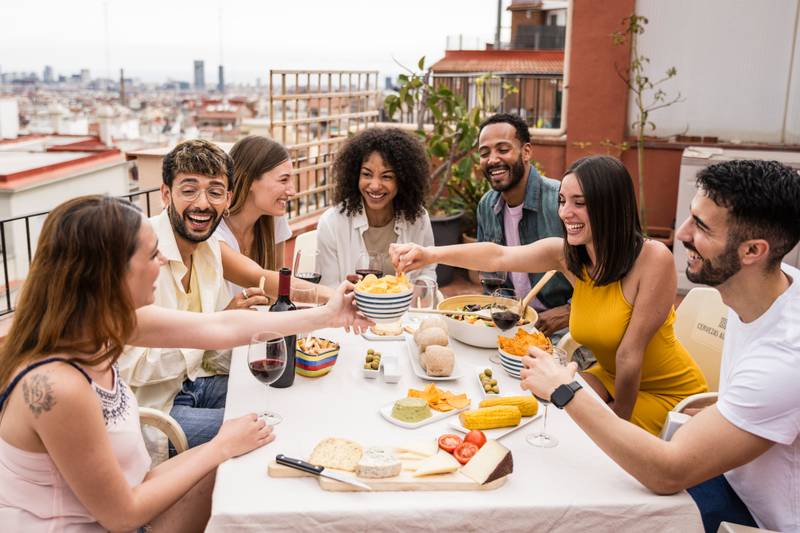 Cheerful group of diverse friends eating and drinking at a terrace table. Young and relaxed people having fun in a rooftop dinner party.