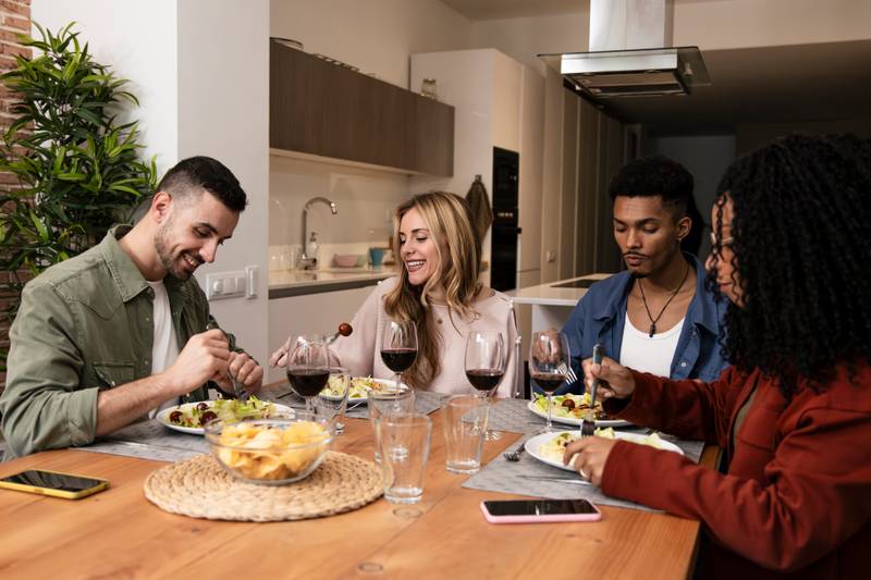 Carefree young people eating and drinking on a modern apartment. Diverse group of relaxed friends having party diner at home. 