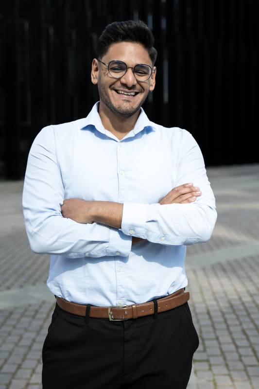 Smiling businessman arms crossed wearing glasses. Cheerful executive laughing in the street.