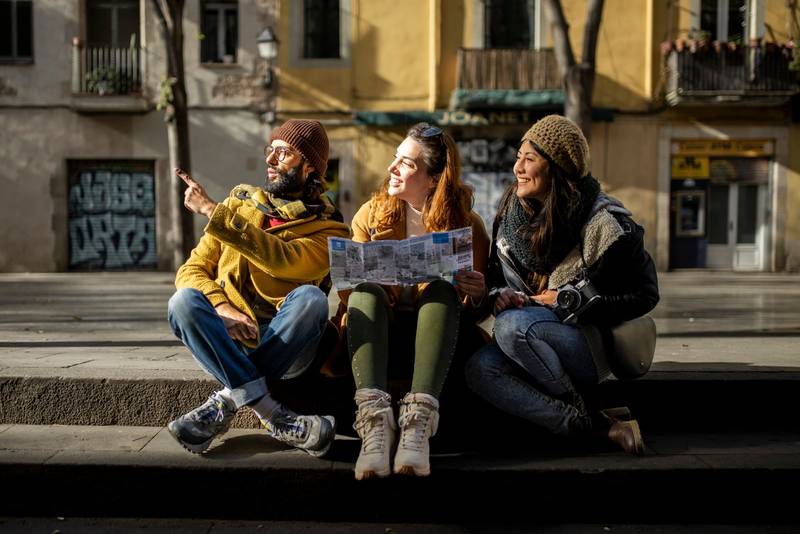 Group of tourists looking a map walking on the street. Three cheerful friends seraching a monument during a city travel