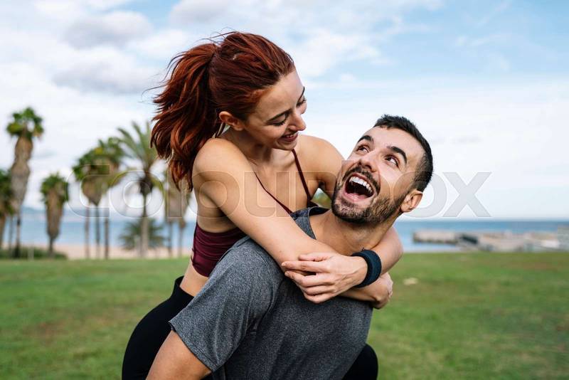 Affectionate young handsome happy fitness couple looking each other outside. Active lovely athletic boyfriend and girlfriend hugging and having fun during training.