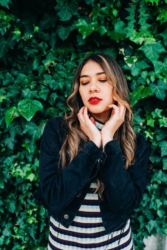 closed eyes young latin woman with blonde wavy hair, wears makeup with red lips