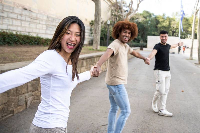 Three diverse and confident friends holding hands together. Multiracial group of people laughing and holding hands in a line. Focus on first woman.