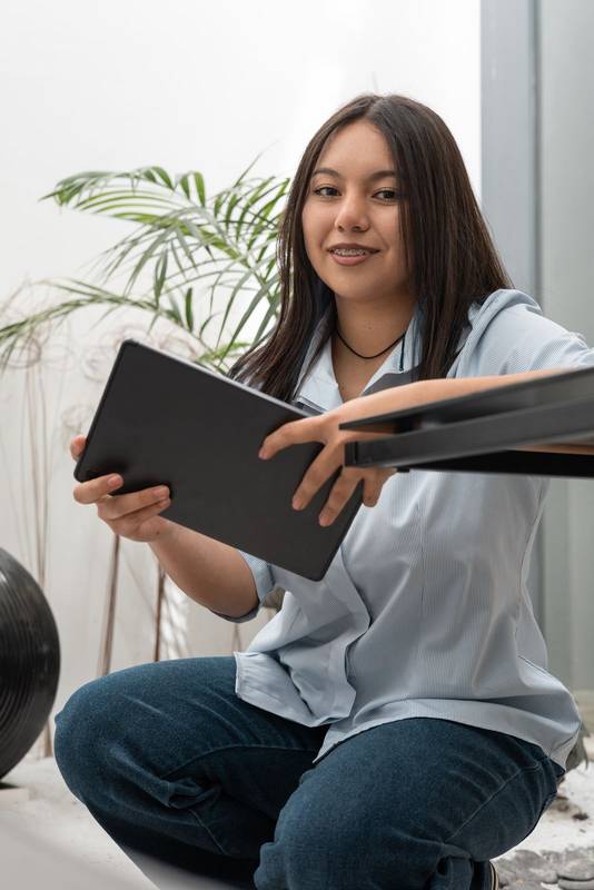 remote tutor in a calm office space prepares her lesson plan on a tablet. Smiling subtly, she enjoys the flexibility of working
