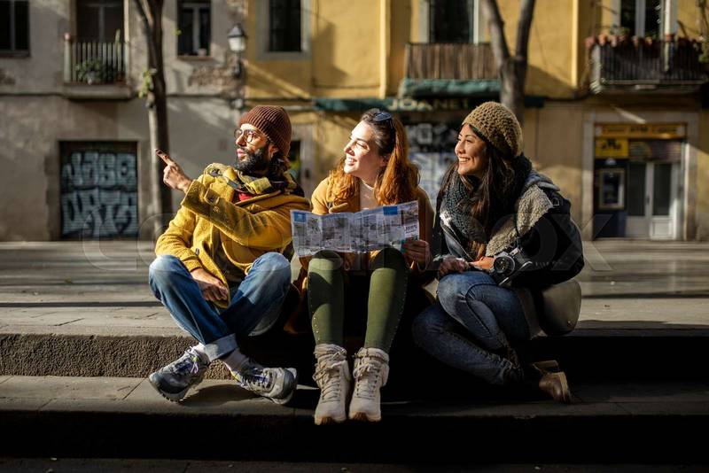 Group of tourists looking a map walking on the street. Three cheerful friends seraching a monument during a city travel